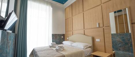 Una habitación de hotel con cama, mesita de noche, espejo y televisor en la pared.