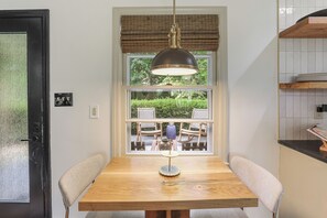 Un comedor con una mesa de madera, dos sillas, una lámpara colgante y vistas al mobiliario exterior a través de una ventana.