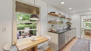 A modern kitchen with a wooden dining table, a built-in oven, and a window with a view of greenery.