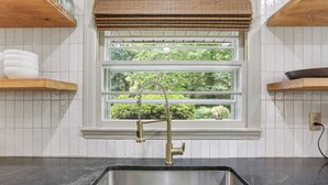 A kitchen with a stainless steel sink, wooden shelves, and a window with a view of greenery.