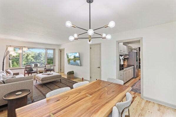 Una sala de estar moderna con una mesa de comedor de madera, sofás y una cocina al fondo.