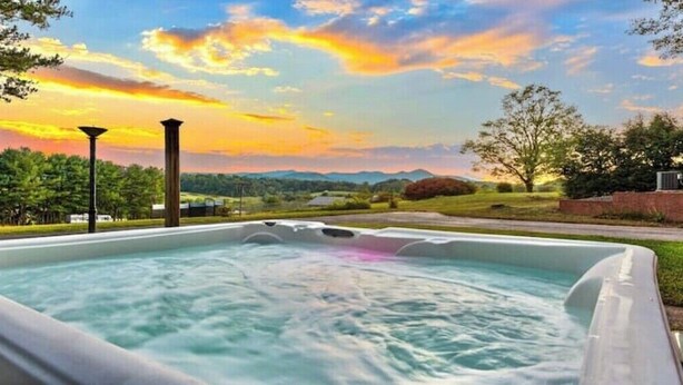A hot tub with a view of a sunset and mountains in the background.