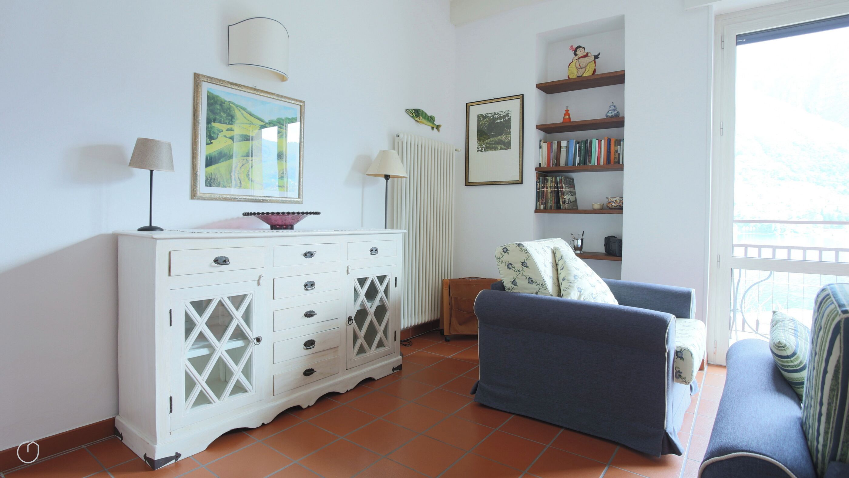 A living room with a white cabinet, a blue sofa, a bookshelf, and a window with a view.