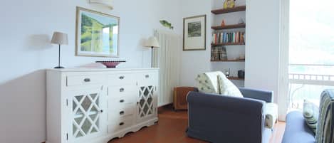 A living room with a white cabinet, a blue sofa, a bookshelf, and a window with a view.
