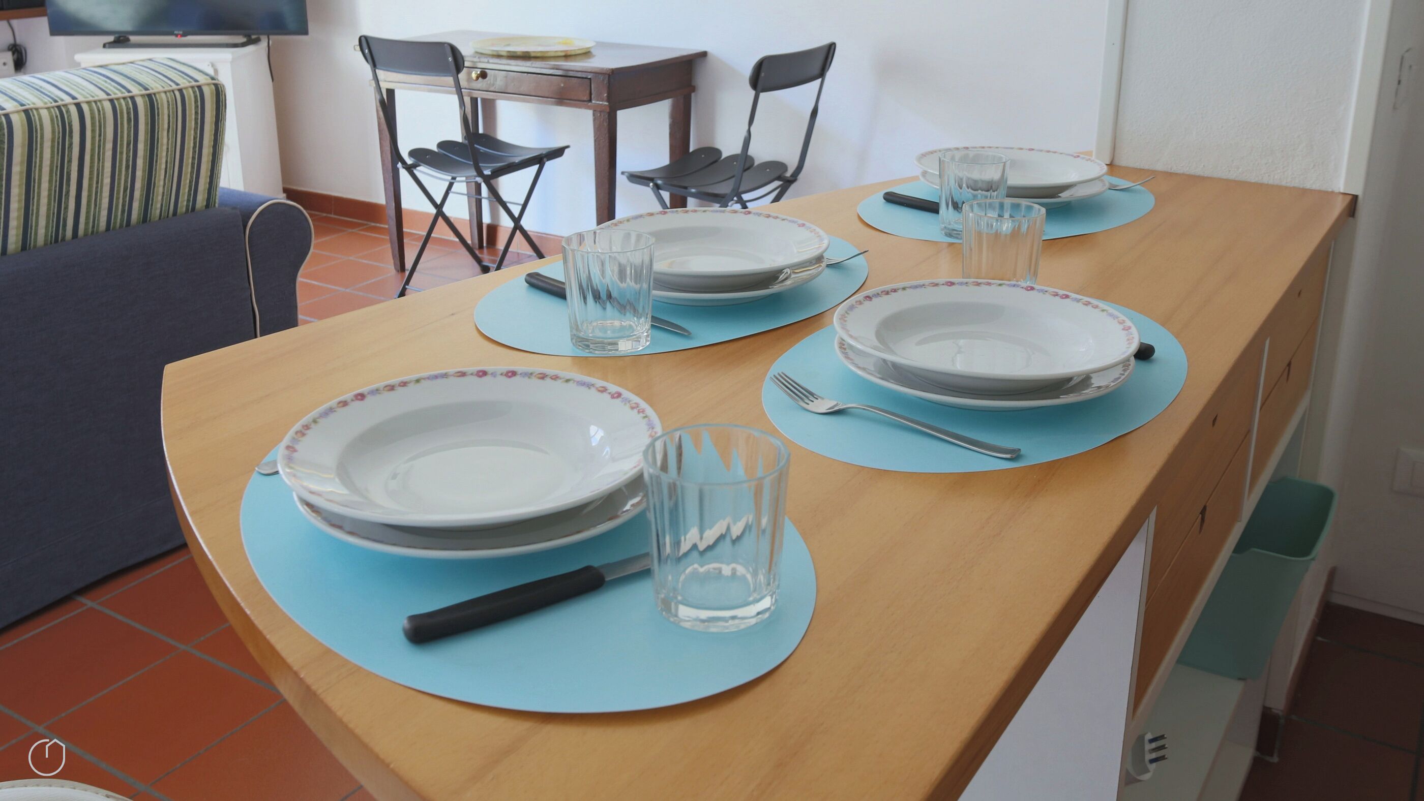 Une table à manger dressée avec des assiettes, des verres et des couverts, entourée de chaises.