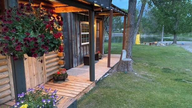 Eine Blockhütte mit einer Holzterrasse, Blumenkästen und Blick auf einen See.