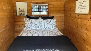 Ein Schlafzimmer in einer Holzhütte mit einem Bett, einem gerahmten Bild eines Wolfes, einem Fenster mit Vorhängen und einem motivierenden Zitat an der Wand.
