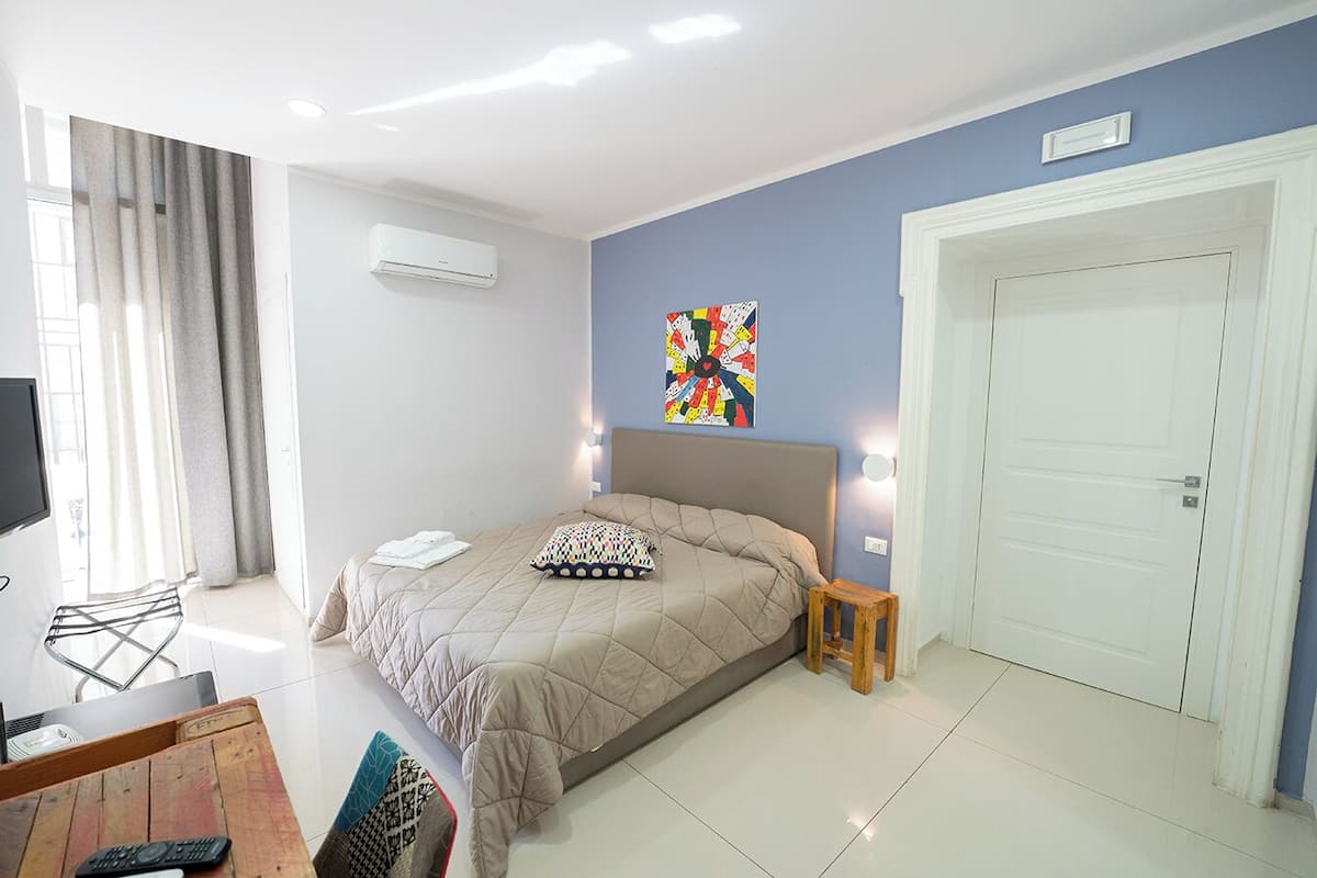 A hotel room with a bed, a television, a chair, a small table, and a door.
