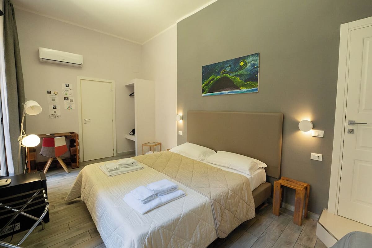 A hotel room with a large bed, a desk, a chair, a lamp, and a painting on the wall.