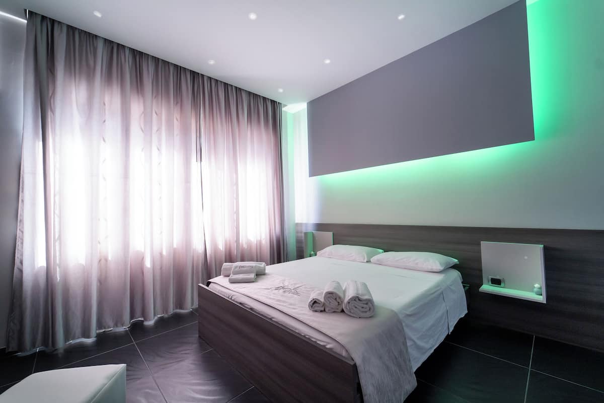 A modern hotel room with a large bed, a bedside table, a nightstand, and a wall-mounted TV.