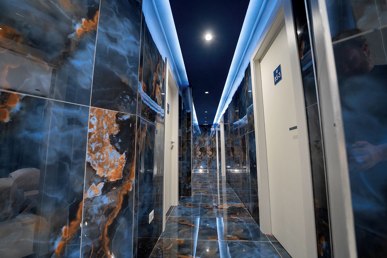 A hallway with marble walls and a glass door, leading to a room with a sign indicating room number 853.