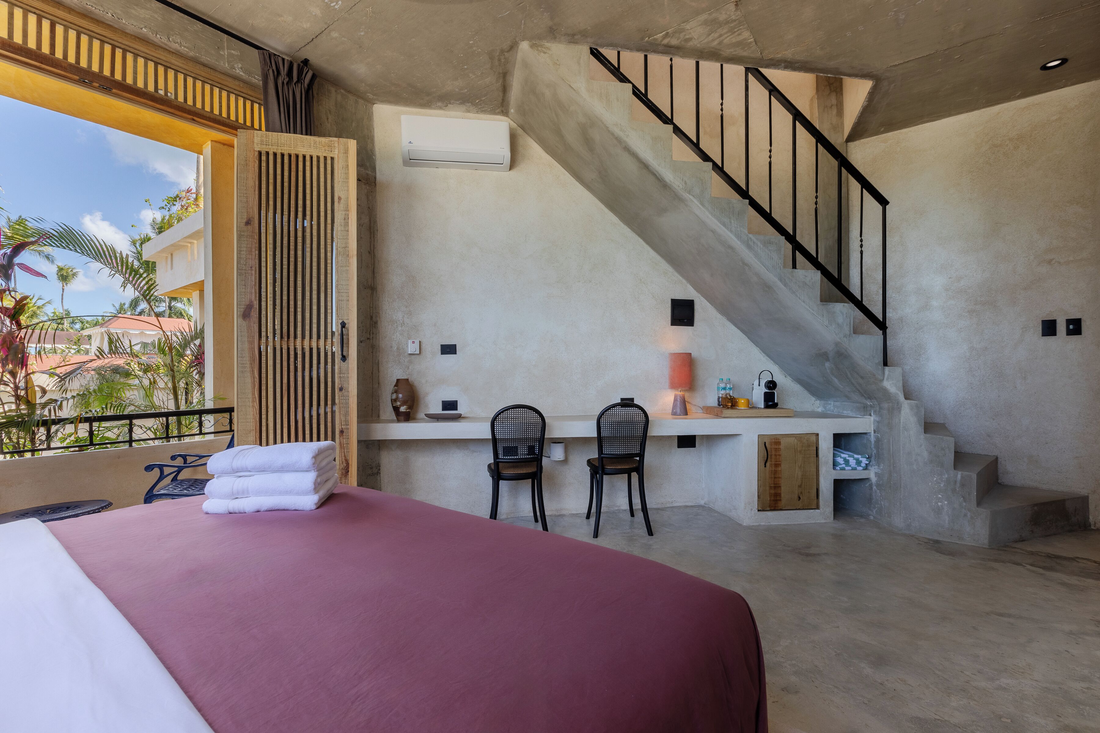 Una habitación de hotel con cama, dos sillas, un escritorio y una escalera.