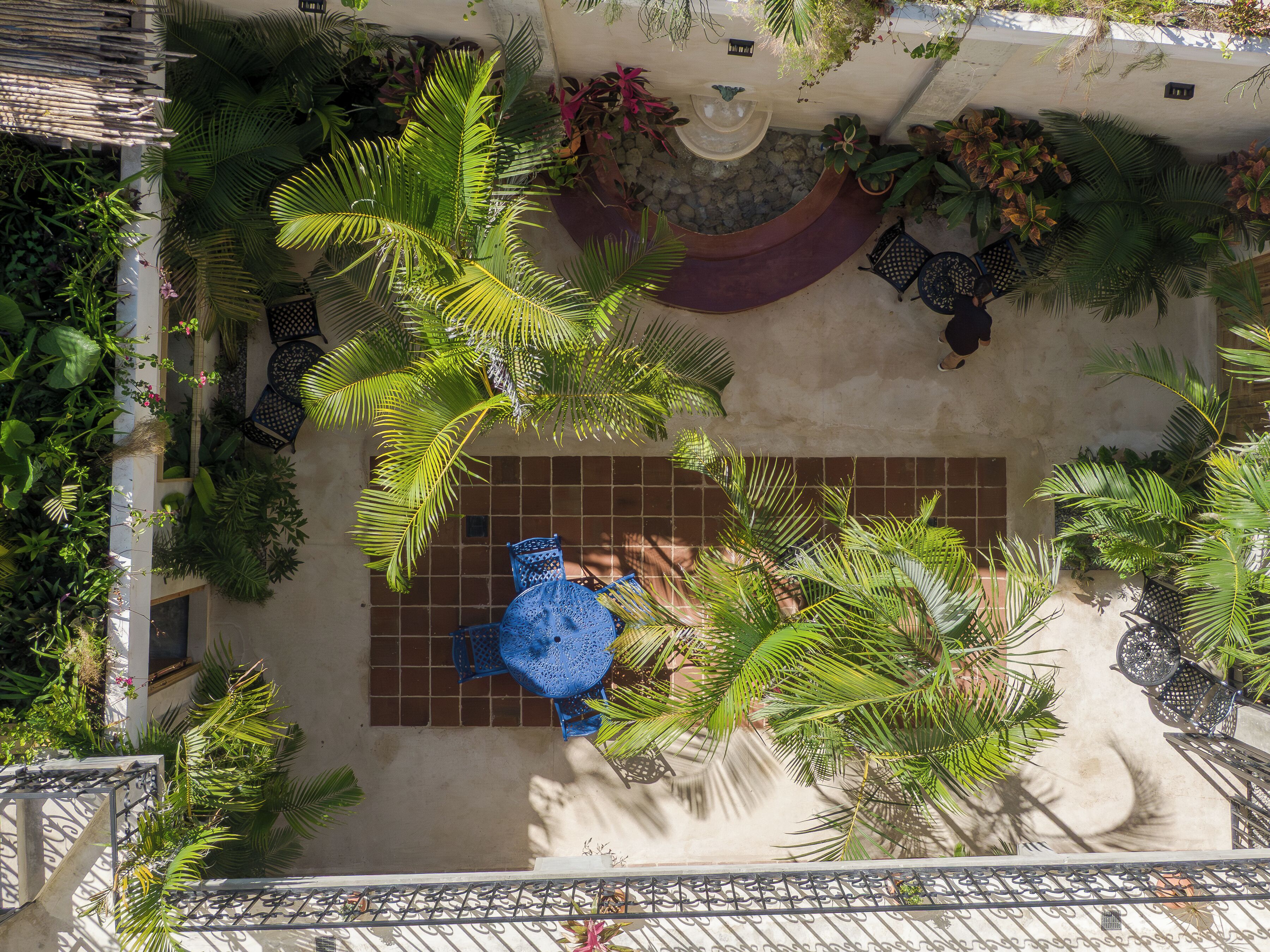 Un jardí al terrat amb taula i para-sol blaus, plantes en testos i un paviment de rajoles.
