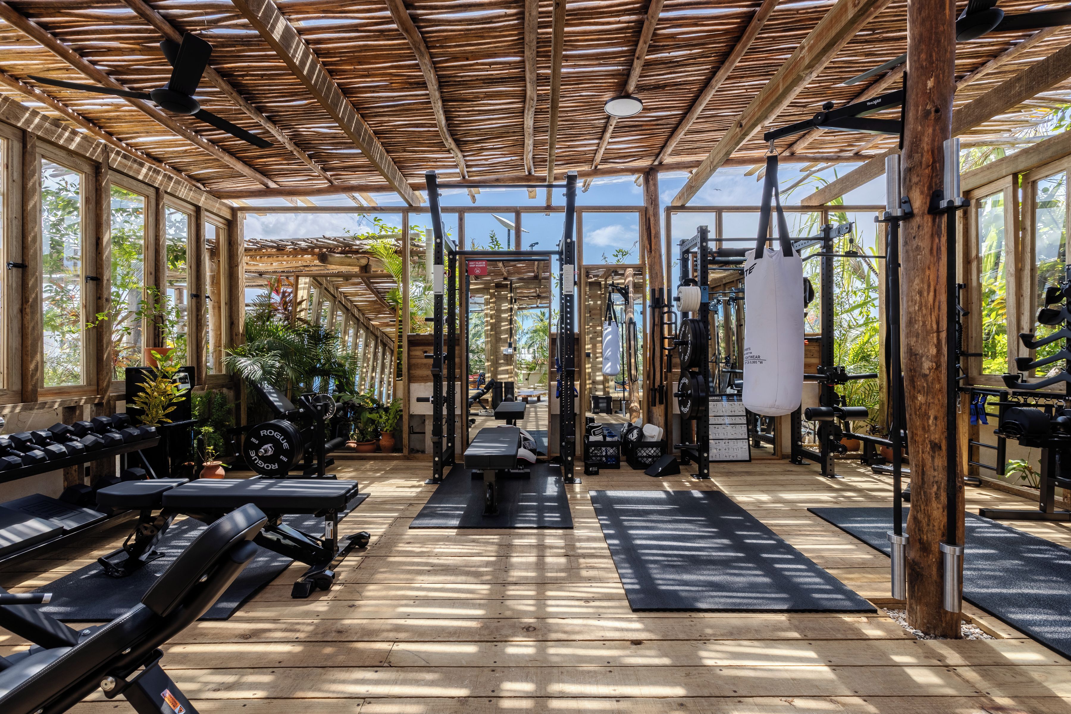 Une salle de sport avec des poutres en bois, du matériel d’exercice et de grandes fenêtres.