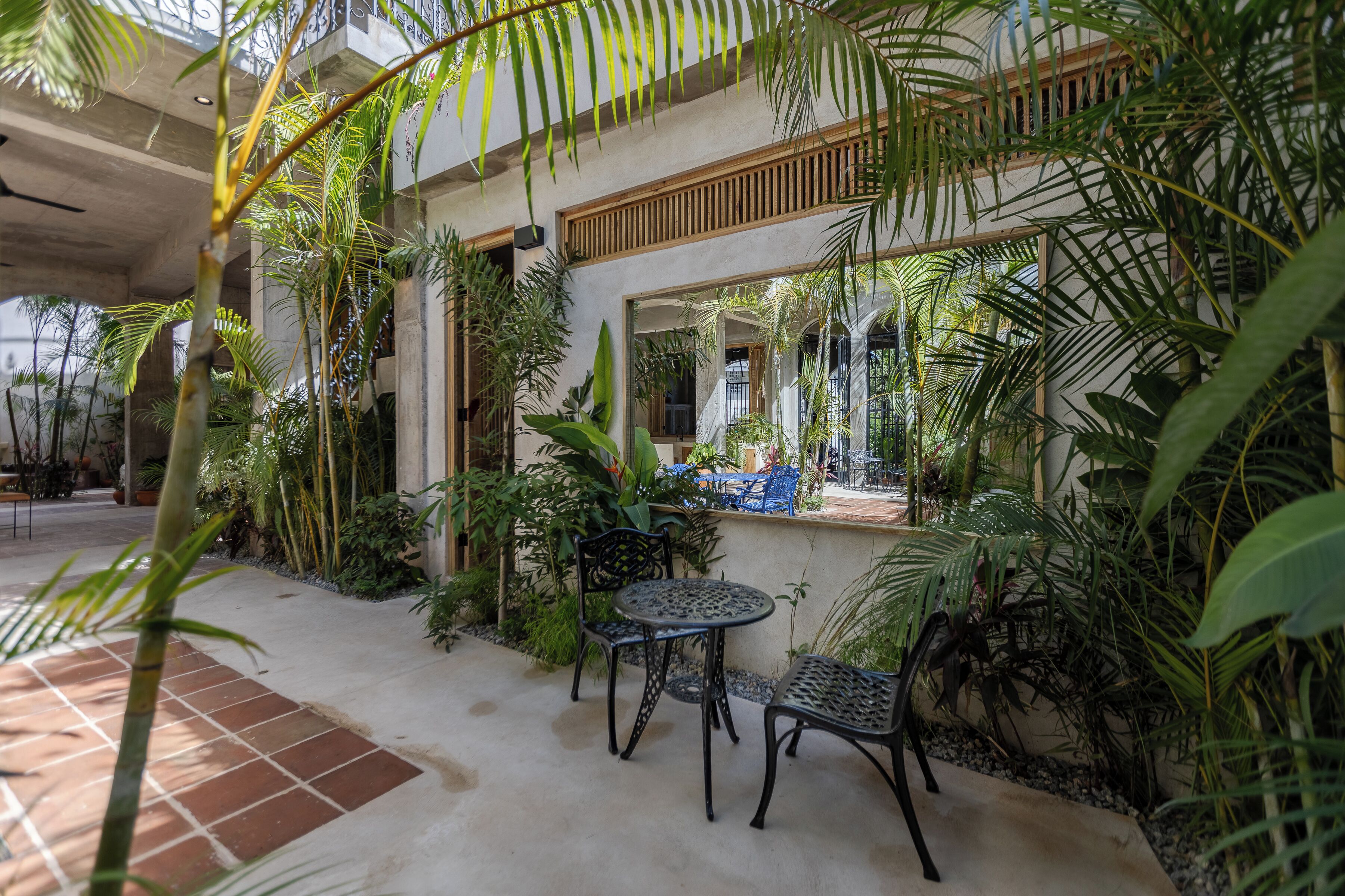 An indoor garden with a patio area featuring a table and chairs, surrounded by various plants and a wooden railing.