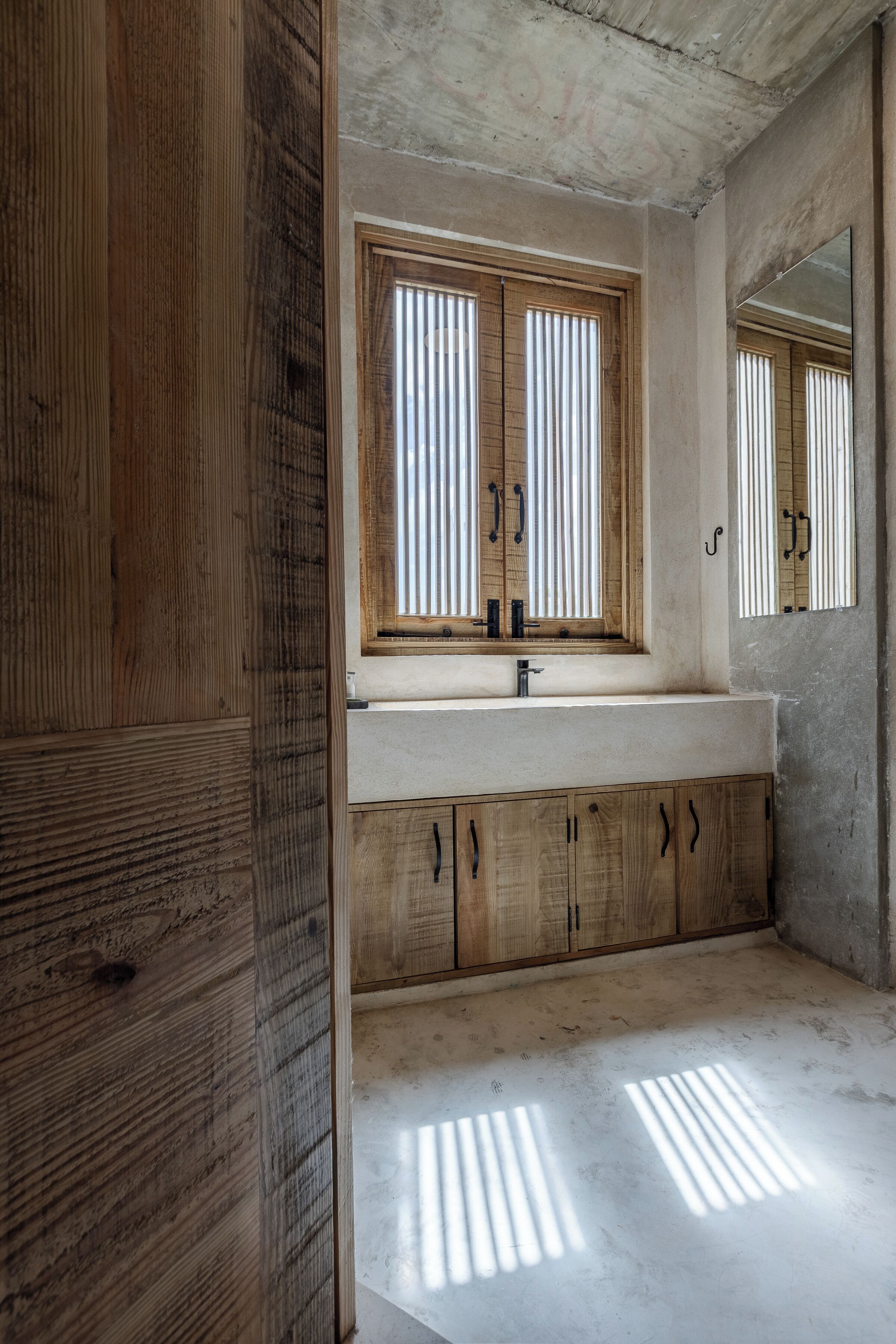 A bathroom with a wooden vanity, a large mirror, and a window with vertical blinds.