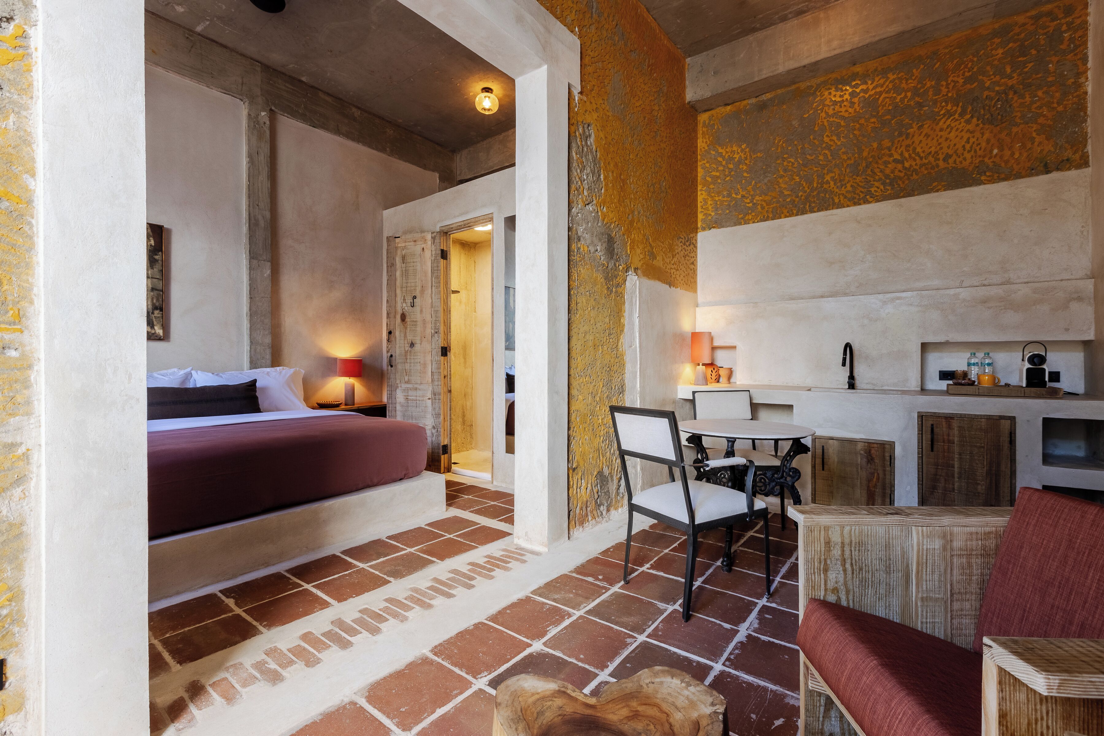 A cozy room with a bed, a small table with chairs, a wooden cabinet, and a tiled floor.