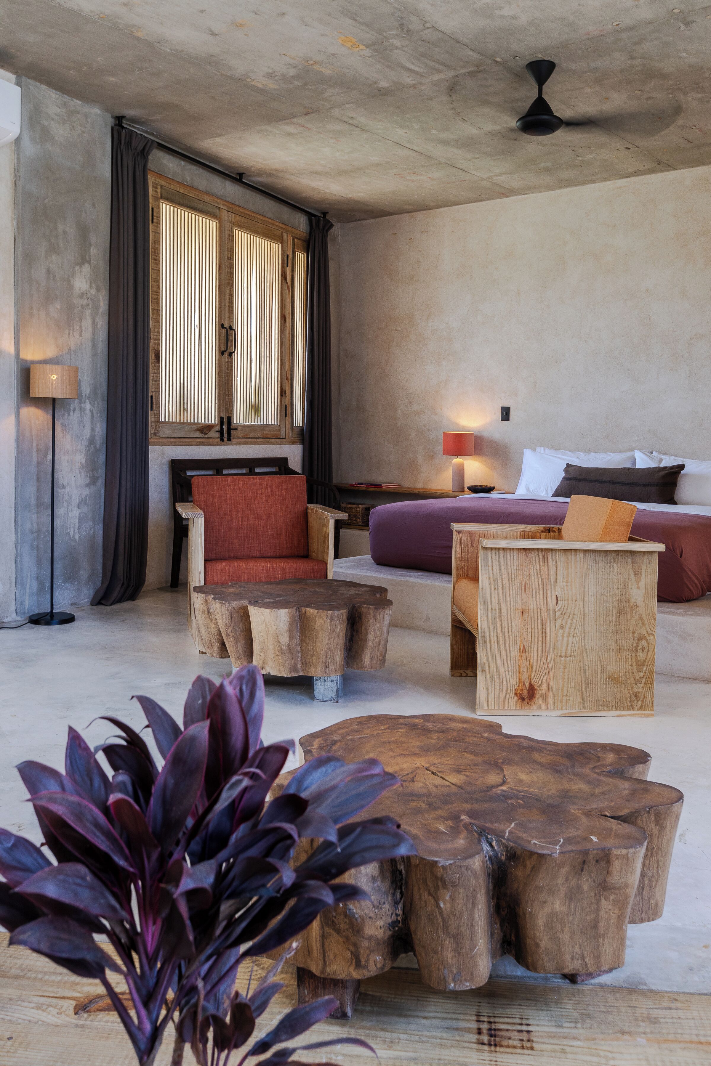 Une pièce avec une table basse en bois, une chaise rouge et un lit recouvert d’une couverture violette.