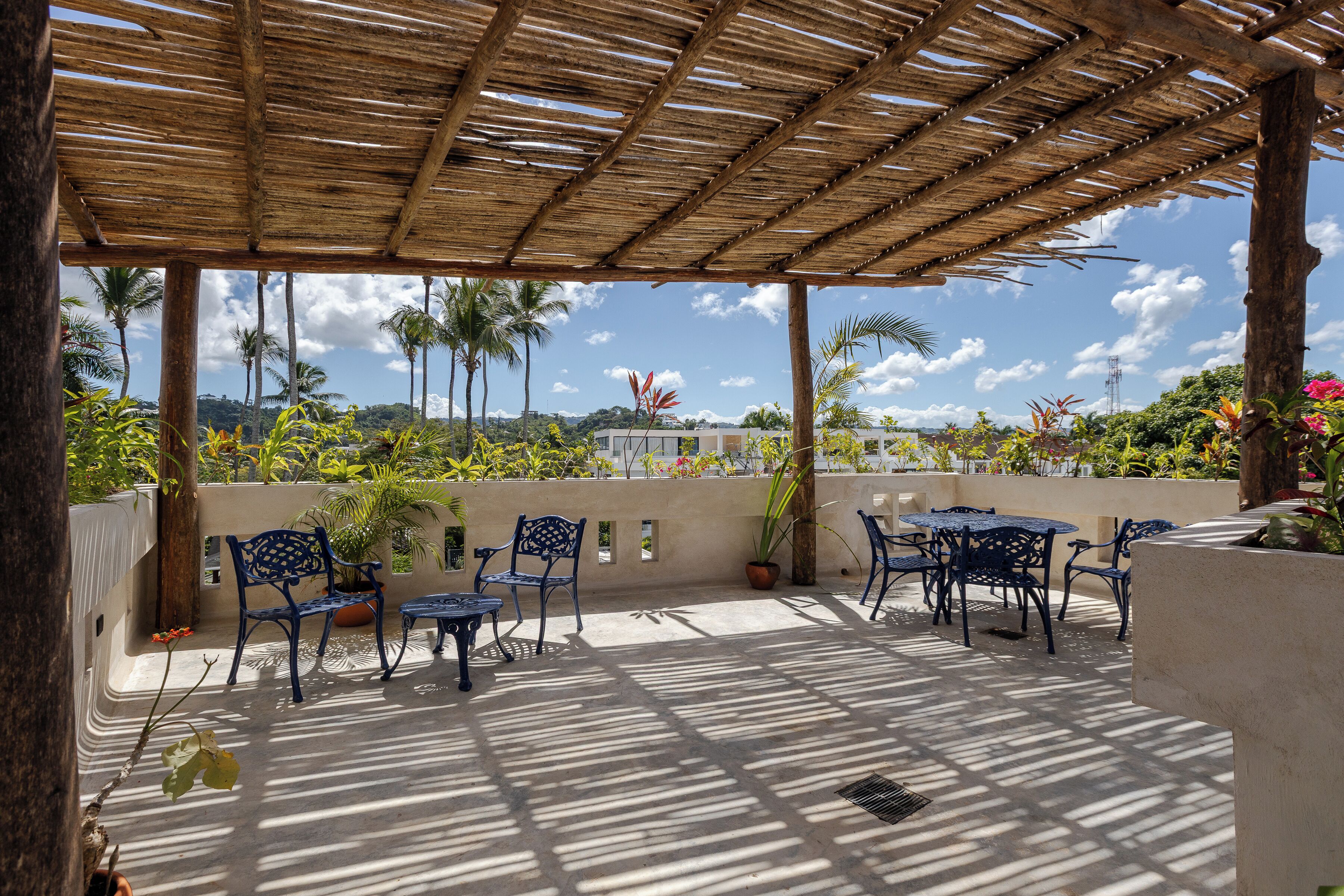 Une terrasse extérieure dotée d’une pergola en bois, de chaises et de tables en métal bleu.