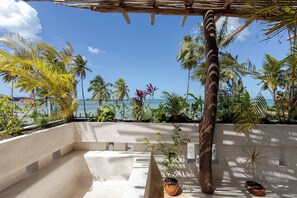A terrace with a view of the sea, surrounded by palm trees and potted plants.