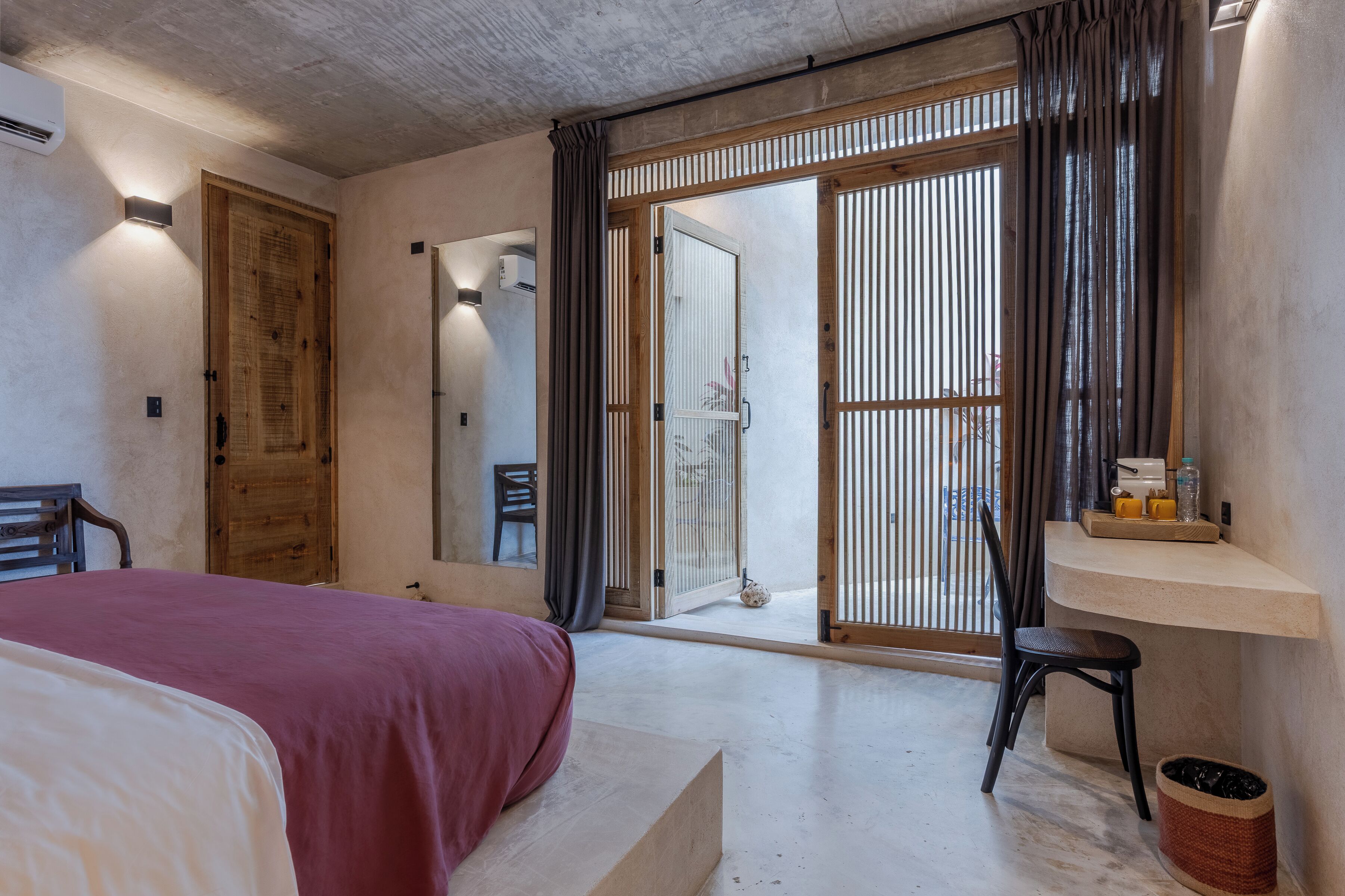 A bedroom with a bed, a desk, a chair, and a sliding glass door leading to a balcony.