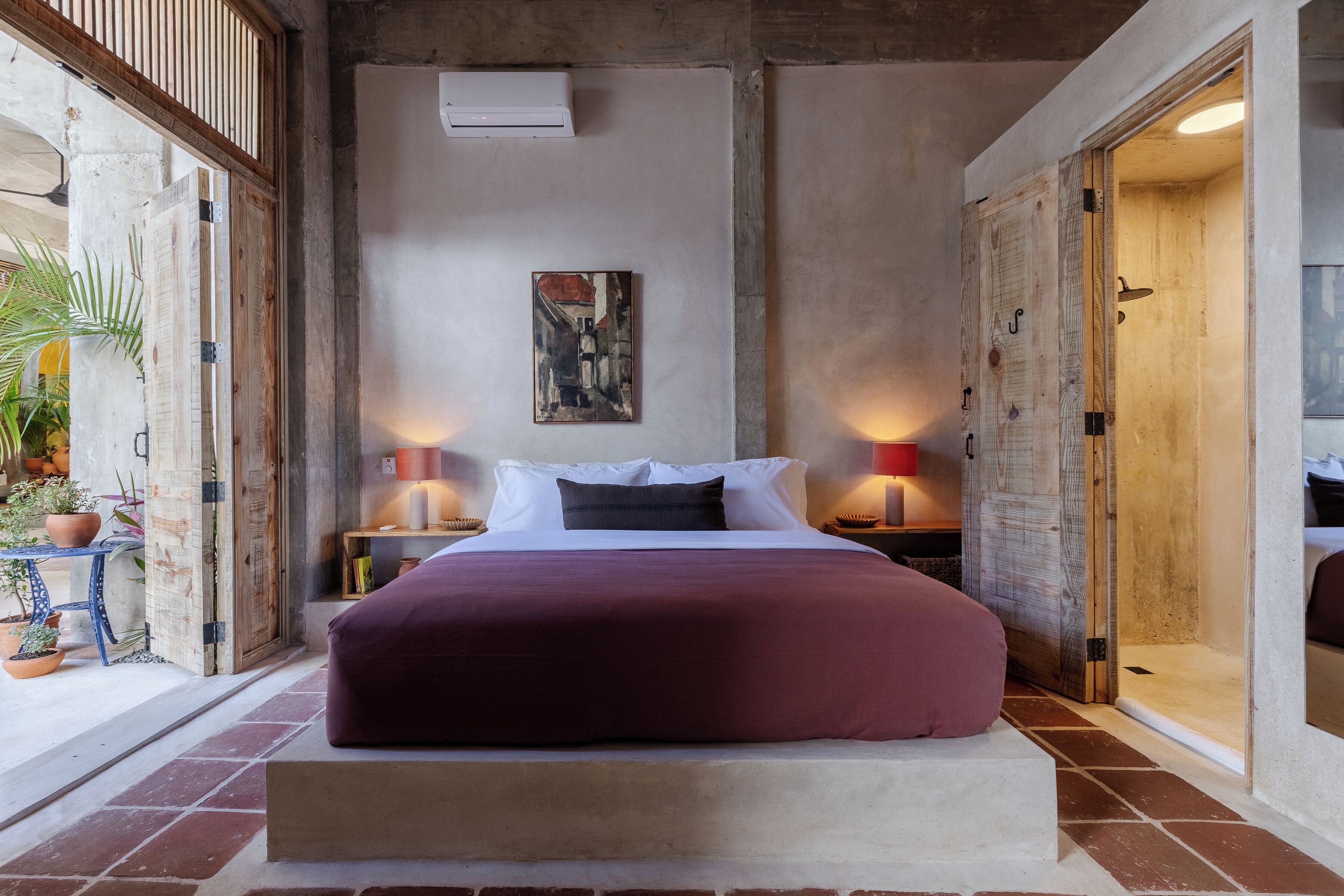 Un dormitori amb un llit gran, dues taules de nit amb làmpades, un quadre a la paret i vista cap a l'exterior a través d'una porta de fusta.