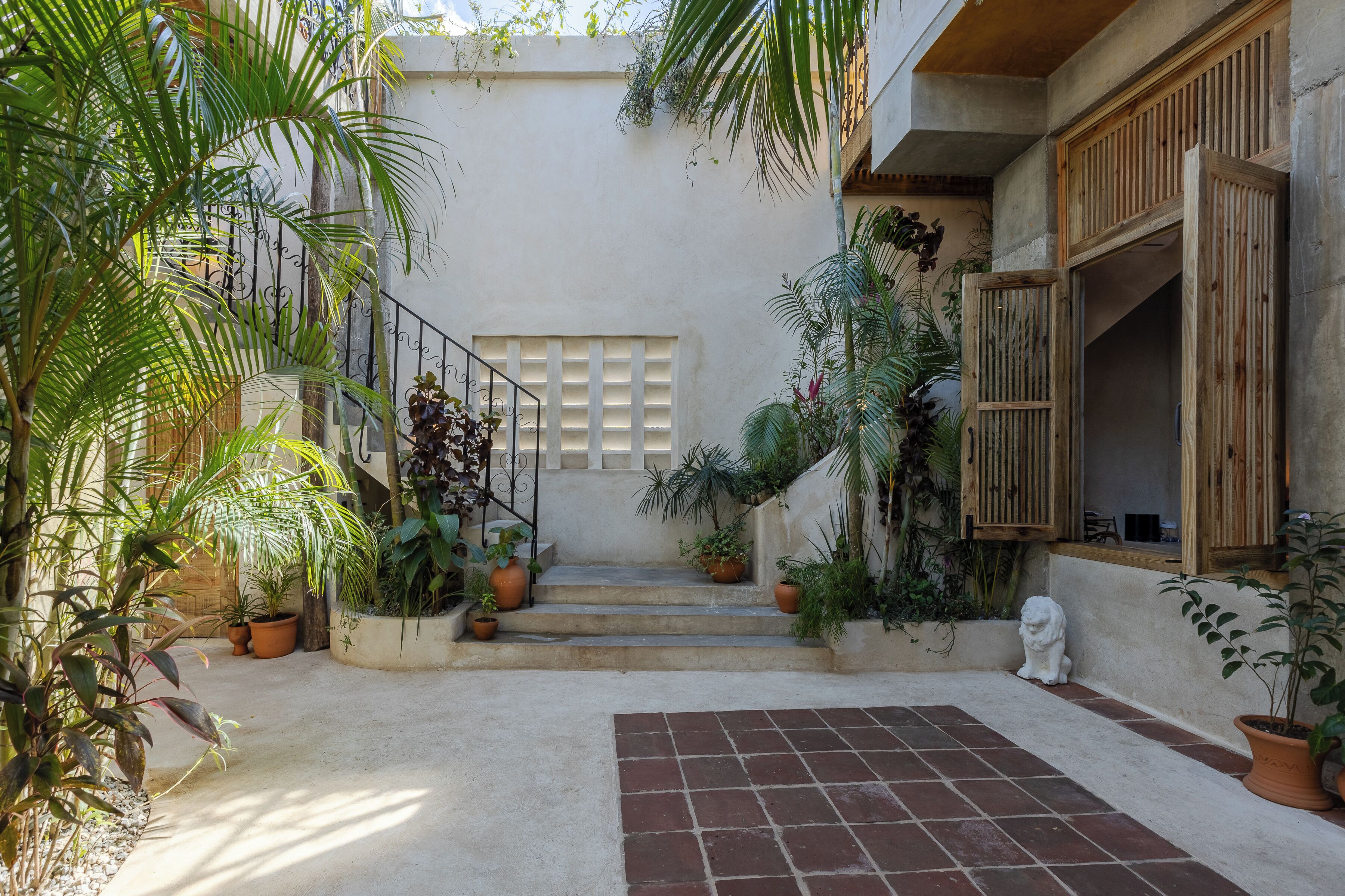 A courtyard with steps leading to a door, surrounded by potted plants and a statue.