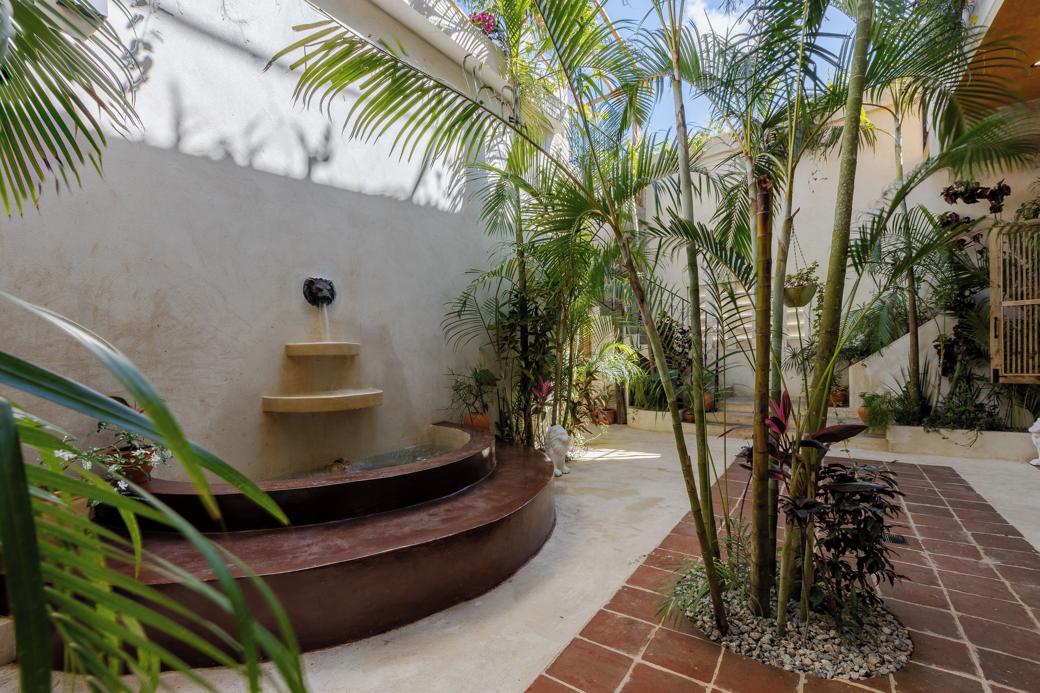 A courtyard with a curved stone bench, potted plants, and a small water feature.