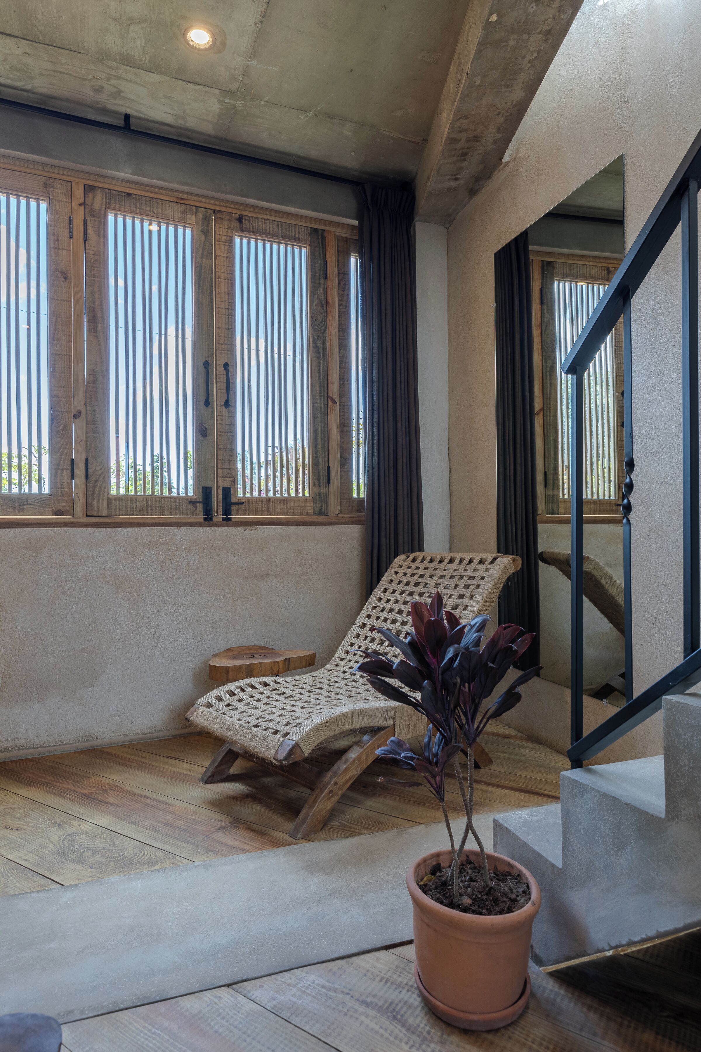 A room with a wooden chair, a potted plant, and a staircase.