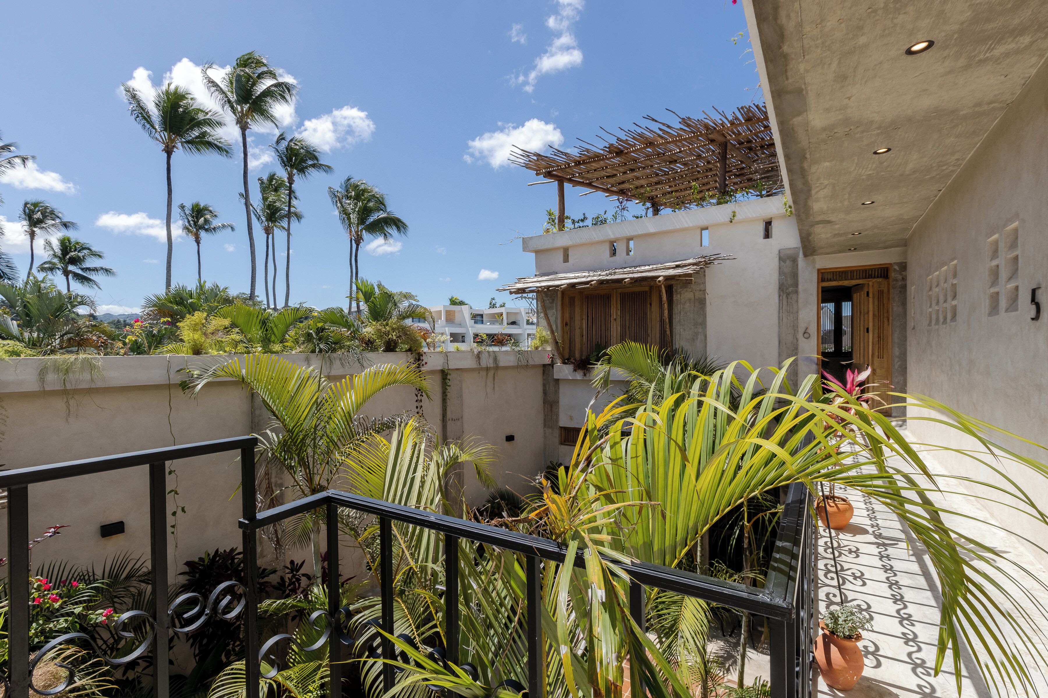 A courtyard with a staircase, potted plants, and a view of palm trees and buildings.