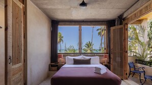 Una camera da letto con un letto grande, vista su palme e oceano, e un balcone con una sedia.