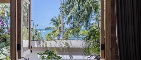 Una habitación con vistas a palmeras y al océano a través de un ventanal grande.