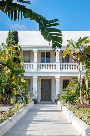 A two-story building with a white facade, a central entrance with a round door, and a balcony with white balustrades.