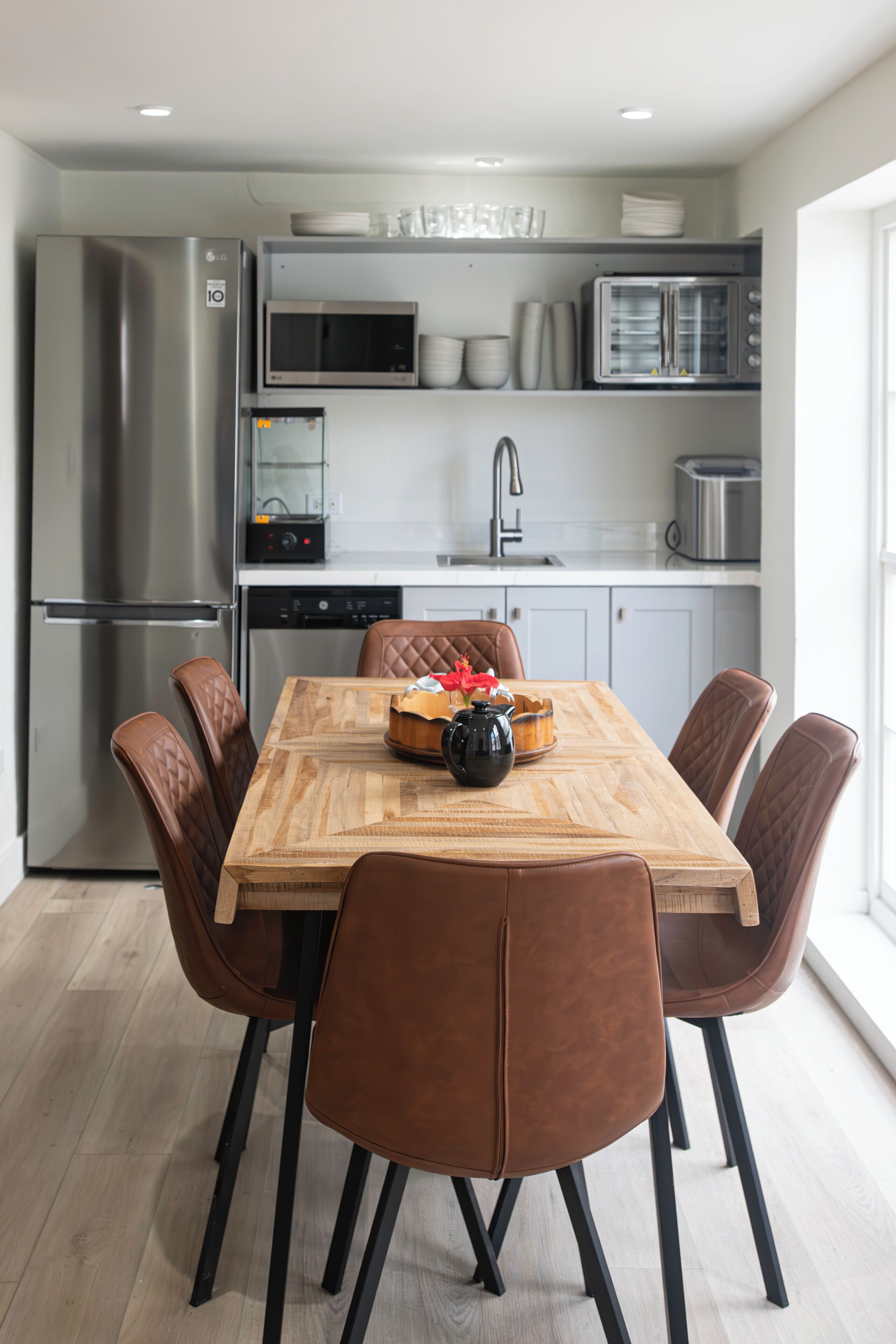 Una cucina moderna con un tavolo da pranzo in legno, sei sedie marroni ed elettrodomestici in acciaio inossidabile, tra cui frigorifero, microonde e forno.