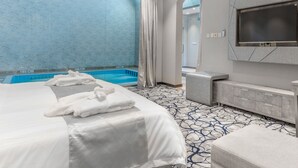 A hotel room with a large bed, a TV, a small seating area, and a view of a pool.