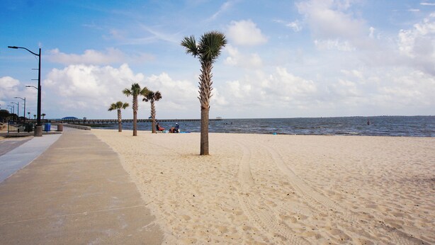 A sandy beach with palm trees and a pier in the background. - Steps to Beach, Downtown 2BR, Pool By WKNDR Getaways (Ocean Springs)