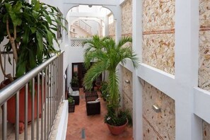 Un estrecho pasillo interior con suelo de baldosas, plantas en macetas y una escalera al fondo.