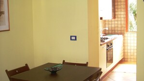 A dining area with a wooden table and chairs, a small bowl on the table, and a kitchen in the background. - VILLA CECILIA- apt. 4 Charming apartment in the heart of Cilento, southern Italy (Pisciotta)