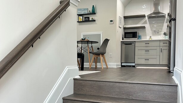 Una cocina moderna con microondas, estufa y refrigerador. Hay una zona de comedor con una mesa y sillas. Una escalera conduce a otro nivel.