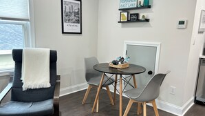 Una sala de estar moderna con un sofá gris, una mesa redonda con sillas, un cuadro con una vista urbana enmarcada y un termostato en la pared.