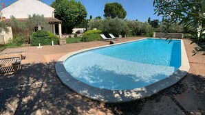 Ein rechteckiger Pool mit geschwungener Kante, umgeben von einer Betonplattform. In der Nähe des Pools befinden sich zwei Liegestühle und ein kleiner Tisch.