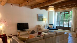 Ein Wohnzimmer mit einer großen Couch, einem Fernseher, einer Stehlampe und einem Fenster mit Vorhängen.