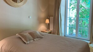 Ein Schlafzimmer mit einem großen Bett, einem runden Spiegel, einer Nachttischlampe und einem Fenster mit Vorhängen.