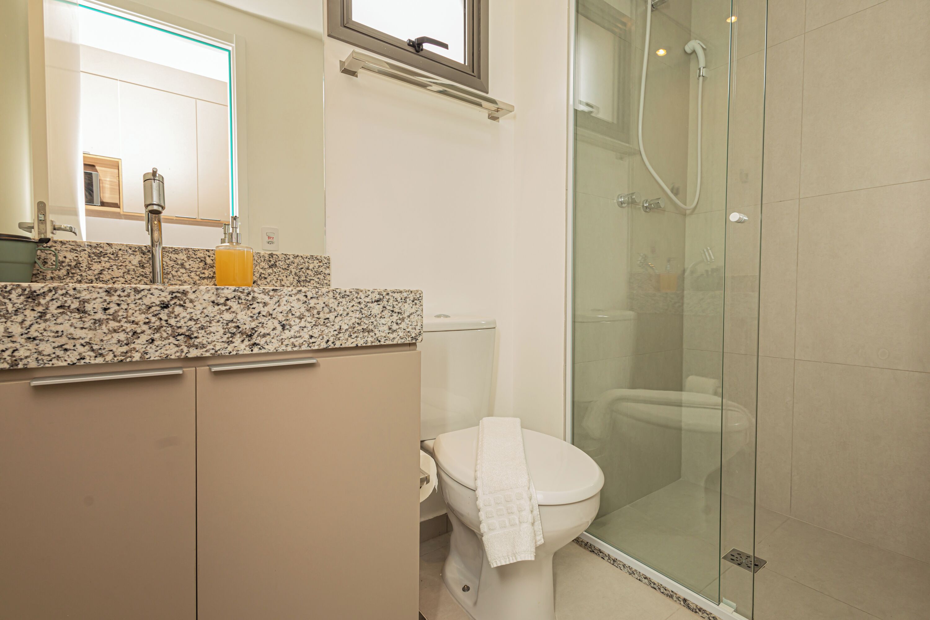 A bathroom with a granite countertop, a toilet, a glass shower enclosure, and a mirror above the sink.