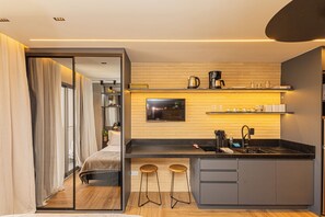 Una cocina moderna con una isla central, taburetes de bar, un televisor de pantalla plana y una cafetera.