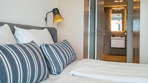 Ein modernes Hotelzimmer mit einem ordentlich bezogenen Bett, einer Nachttischlampe und Blick ins Badezimmer.
