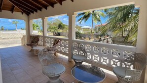 Un espace extérieur abrité, aménagé avec des meubles en osier et offrant une vue sur la plage.