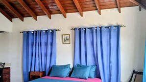 Une chambre à coucher avec un lit, des rideaux bleus, un plafond en bois et un sol carrelé.