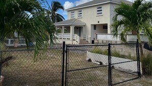 Une maison à deux étages avec une cour clôturée, des palmiers et un ciel dégagé.