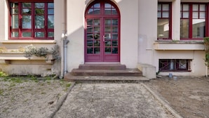 En byggnad med en central, välvd entré, en röd dörr och flera fönster med röda ramar.